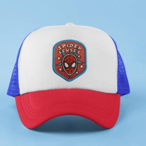 May include: A red, white, and blue trucker hat with a Spidey Senses emblem. The hat features a white front panel with a Spiderman logo, a red curved brim, and blue mesh sides and back.