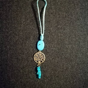 以下が含まれることがあります： ターコイズとゴールドのネックレス。生命の木のペンダントとターコイズビーズが飾られています。