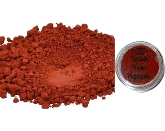 May include: A pile of reddish-brown pigment next to a small, clear jar. The jar contains the same pigment and has the words "Italian Brown Pigment" printed on it. The pigment appears to be finely ground and has a matte finish.
