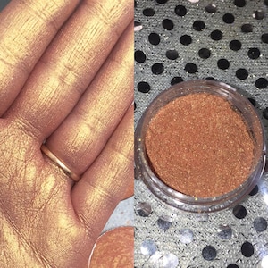 May include: A small jar of loose gold glitter with a shimmery finish. The glitter is shown on a hand and in the jar.