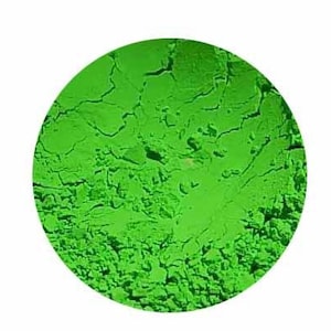 May include: A close-up of a bright green powder, contained within a circular shape. The powder has a textured, slightly cracked appearance, with variations in tone. The overall effect is a vibrant, solid color.