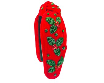 Op de afbeelding: Rood fluwelen hoofdband met een geknoopt ontwerp en groene en rode parelversieringen van hulstbladeren.