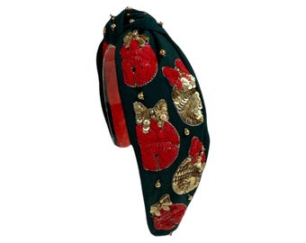 Op de afbeelding: Een donkergroen geknoopt hoofdband met rode en gouden paillettenversieringen. Het hoofdband is versierd met een herhalend patroon van rode en gouden pailletten.