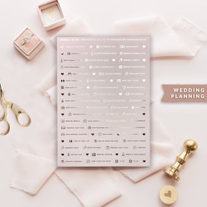 May include: A sheet of rose gold foil stickers with white text for wedding planning. The stickers feature icons and text such as "Book Venue", "Order Dress", "Wedding Website", "Guest List", "Reception Music", "Wedding Program", and "Thank You Notes".