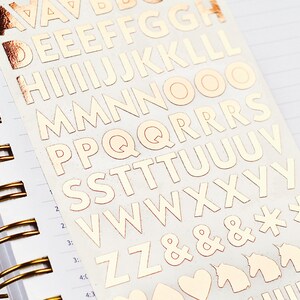 Op de afbeelding: Een vel met gouden letter stickers met de letters A tot en met Z, ampersands, sterretjes, eenhoorns, harten en vraagtekens.