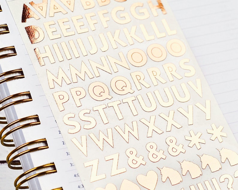 Op de afbeelding: Een vel met gouden letter stickers met de letters A tot en met Z, ampersands, sterretjes, eenhoorns, harten en vraagtekens.