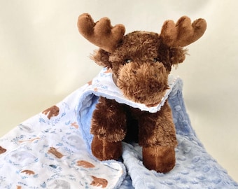 May include: A brown plush moose toy is nestled in a blue and white baby blanket. The blanket has a white side with a pattern of woodland animals and a blue side with a textured, quilted pattern.