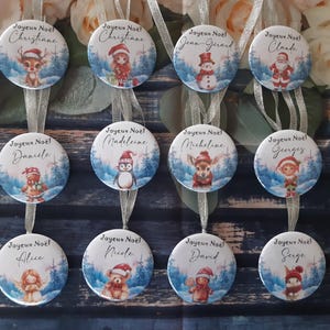 Peut inclure: Ronds de Noël ornés d'illustrations festives et de noms tels que 'Christiane' et 'Jean-Gerard'. Chaque ornement affiche 'Joyeux Noël' et est orné d'un ruban argenté pour être suspendu. Les motifs incluent un renne et un bonhomme de neige.