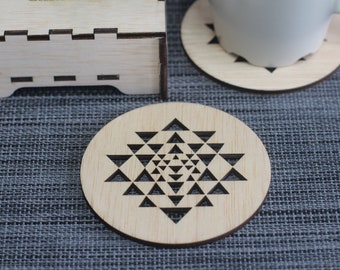 May include: A set of four wooden coasters with a geometric design. The coasters are made of light brown wood and feature a black geometric pattern. The coasters are in a box with the text "Kakya Creative Studio" printed on the front.