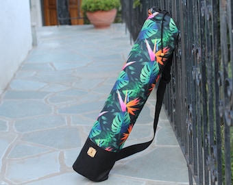 Puede incluir: Una bolsa negra para esterilla de yoga con estampado tropical de hojas verdes y flores naranjas y rosas. La bolsa tiene una correa negra ajustable.