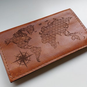 Puede incluir: Un portapasaporte de cuero marrón con un diseño de mapa del mundo y brújula.