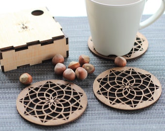May include: Four wooden coasters with a geometric design, a white mug, and a small wooden box with a bee design. The coasters are on a gray textured surface.
