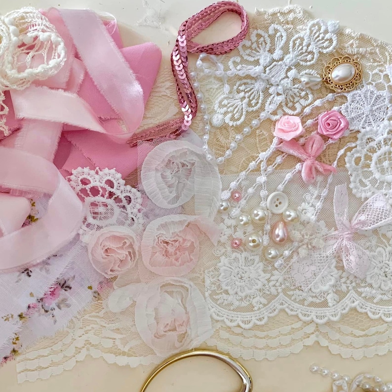 May include: A collection of pink and white lace, ribbon, and embellishments. The lace is delicate and intricate, with a floral pattern. The ribbon is soft and silky, and the embellishments are sparkly and glamorous.