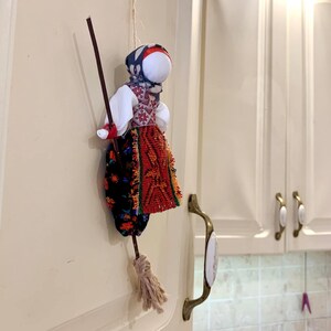 May include: A handmade rag doll with a red, white, and blue dress and a broom. The doll is hanging on a white cabinet door.