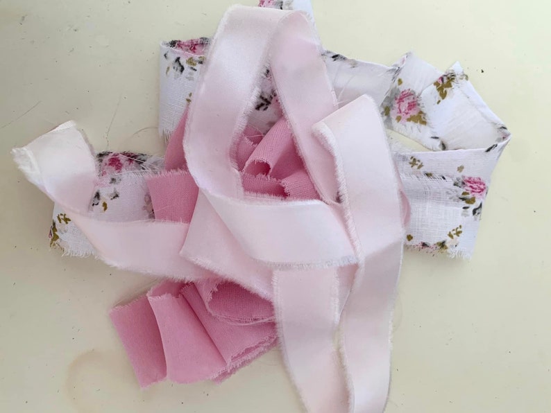 May include: A collection of pink and white fabric scraps with a floral pattern. The fabric is frayed and has a rustic look.