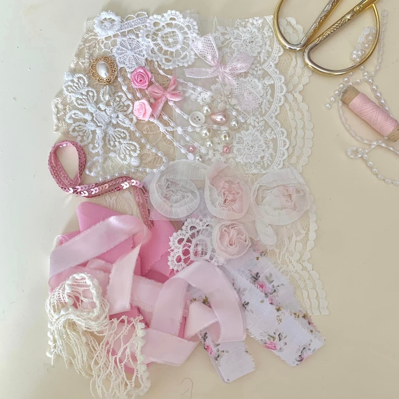 May include: A collection of pink and white lace, ribbon, and fabric scraps for crafting. The scraps include floral designs, sequins, and a pearl-like embellishment.