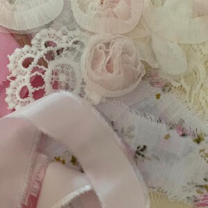 May include: A close-up of a collection of white and pink lace fabric with a pink satin ribbon. The lace has a floral design and the ribbon is curled.