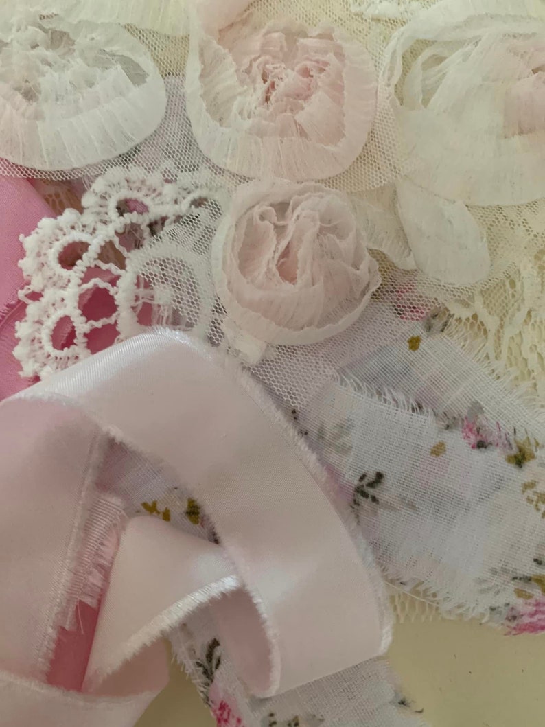 May include: A close-up of a collection of white and pink lace fabric with a pink satin ribbon. The lace has a floral design and the ribbon is curled.