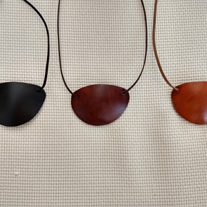 May include: Three leather eye patches on cords, one black, one brown, and one tan.