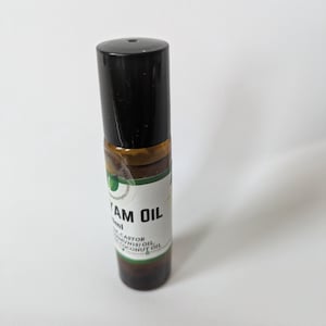 Könnte beinhalten: Eine braune Glasflasche mit einem schwarzen Roll-on-Verschluss. Die Flasche ist mit "Y AM OIL" beschriftet und listet die Inhaltsstoffe auf: "Castor, Munis Oil, Coconut Oil".