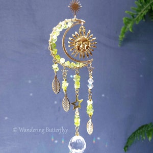 May include: A gold crescent moon suncatcher with green and clear beads, a gold sun charm, and a crystal prism hanging from the bottom. The suncatcher is decorated with gold stars and leaves.