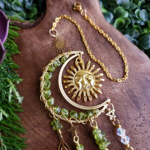 May include: Gold sun and moon dreamcatcher with green peridot stones and gold stars hanging from it.