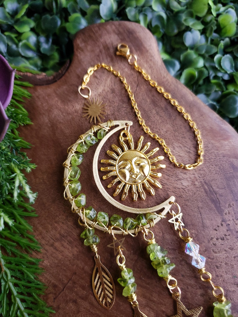 May include: Gold sun and moon dreamcatcher with green peridot stones and gold stars hanging from it.