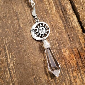 May include: A silver charm necklace with a clear crystal pendant. The charm features a sun and moon design with a face on the sun.