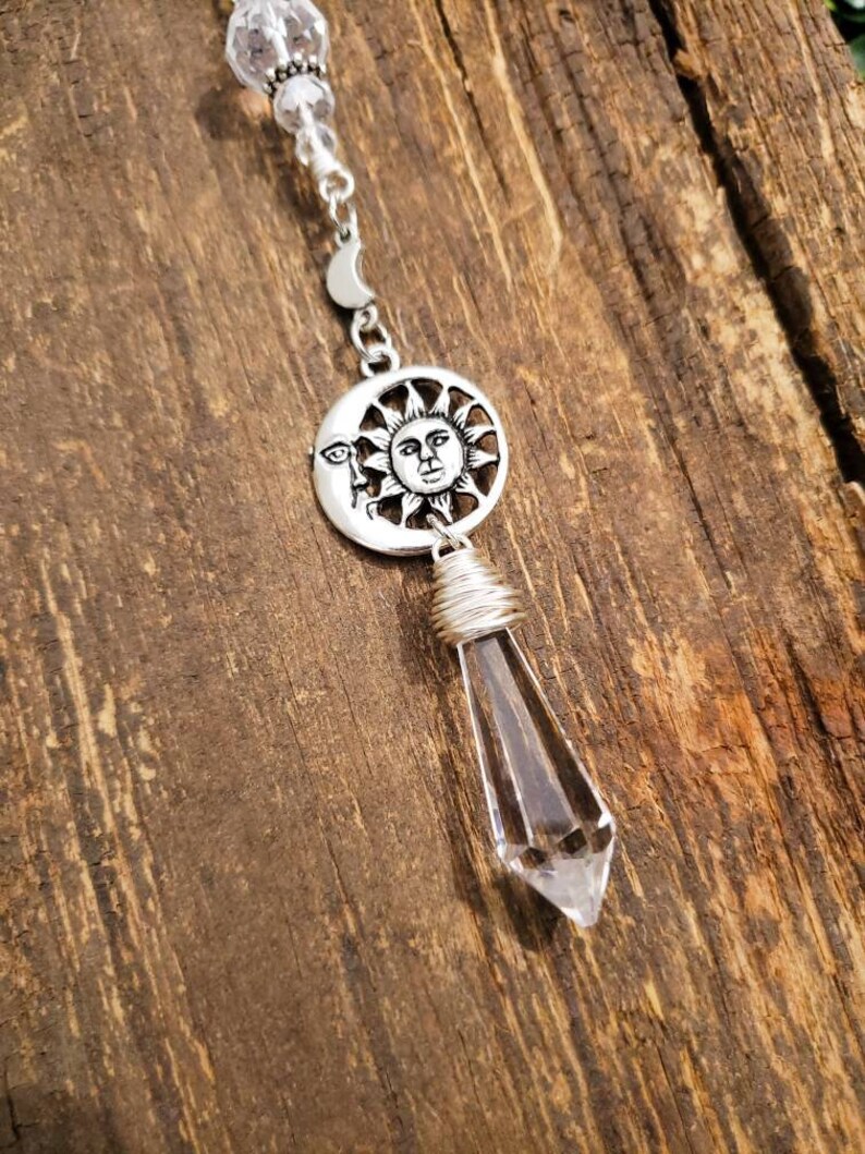 May include: A silver charm necklace with a clear crystal pendant. The charm features a sun and moon design with a face on the sun.