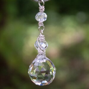 May include: A silver chain with a crystal pendant. The pendant is a large, faceted crystal ball with a smaller crystal bead above it.