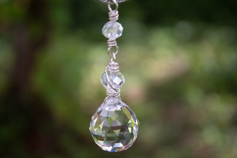 May include: A silver chain with a crystal pendant. The pendant is a large, faceted crystal ball with a smaller crystal bead above it.