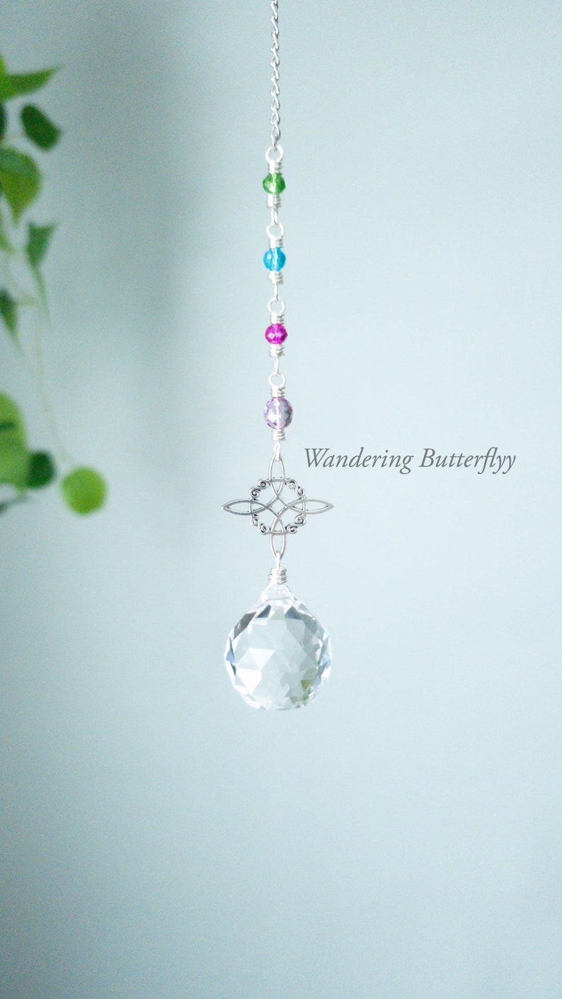 May include: A crystal suncatcher with a clear crystal ball, a silver metal design, and a chain of colorful beads. The beads are green, blue, pink, and purple. The text "Wandering Butterfly" is visible in the image.