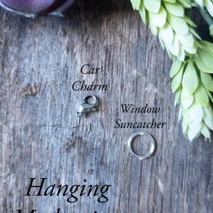 May include: Two different hanging mechanisms for a car charm or window suncatcher. The first is a silver lobster claw clasp, and the second is a silver jump ring. The text "Hanging Mechanism Styles" is written below the two mechanisms.