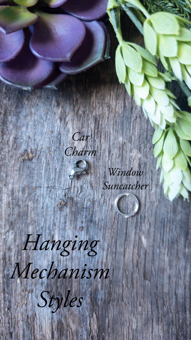 May include: Two different hanging mechanisms for a car charm or window suncatcher. The first is a silver lobster claw clasp, and the second is a silver jump ring. The text "Hanging Mechanism Styles" is written below the two mechanisms.
