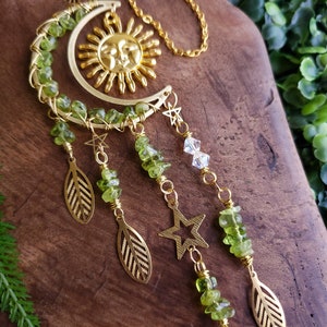 May include: A gold sun and moon crescent charm with green peridot beads and gold leaves and stars hanging from it.