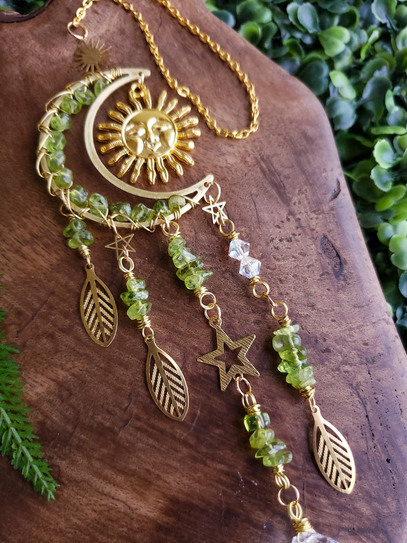 May include: A gold sun and moon crescent charm with green peridot beads and gold leaves and stars hanging from it.