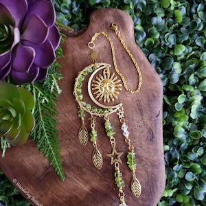 May include: Gold sun and moon charm with green crystals and gold leaves hanging from a crystal prism.