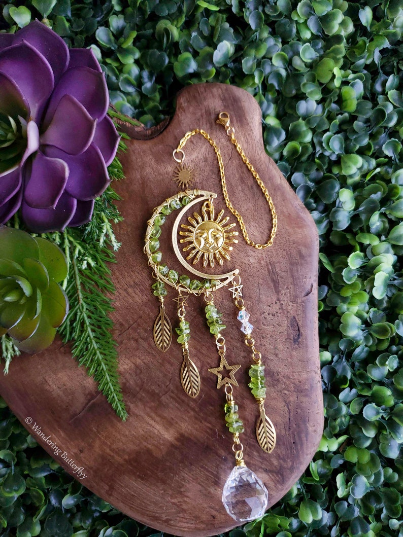 May include: Gold sun and moon charm with green crystals and gold leaves hanging from a crystal prism.
