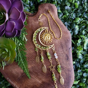 May include: A gold sun and moon suncatcher with green aventurine beads and a clear crystal prism hanging from it. The suncatcher is hanging from a gold chain.