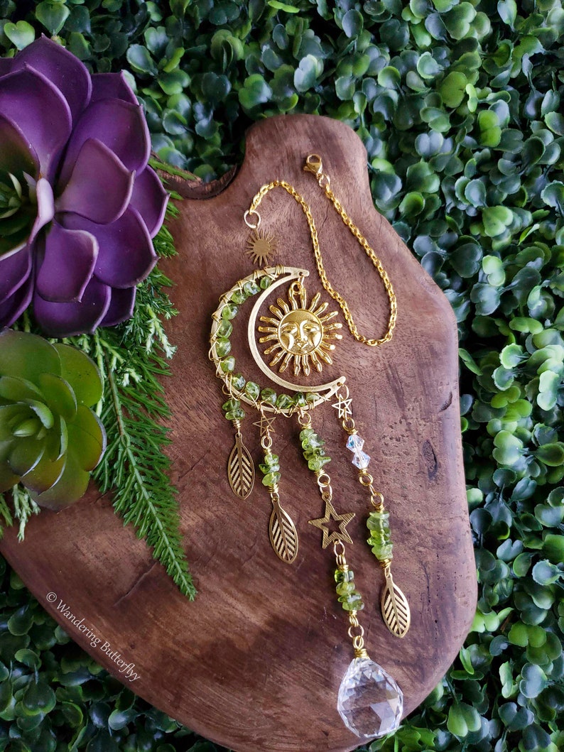May include: A gold sun and moon suncatcher with green aventurine beads and a clear crystal prism hanging from it. The suncatcher is hanging from a gold chain.