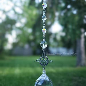 May include: A hanging crystal suncatcher with a clear, faceted crystal ball at the bottom. The suncatcher has a silver chain with clear and iridescent beads, and a decorative Celtic knot. The text "Wandering Butterflyy" is visible.