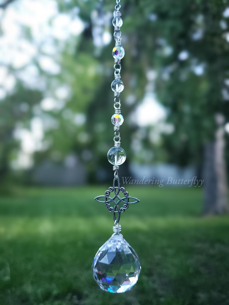 May include: A hanging crystal suncatcher with a clear, faceted crystal ball at the bottom. The suncatcher has a silver chain with clear and iridescent beads, and a decorative Celtic knot. The text "Wandering Butterflyy" is visible.