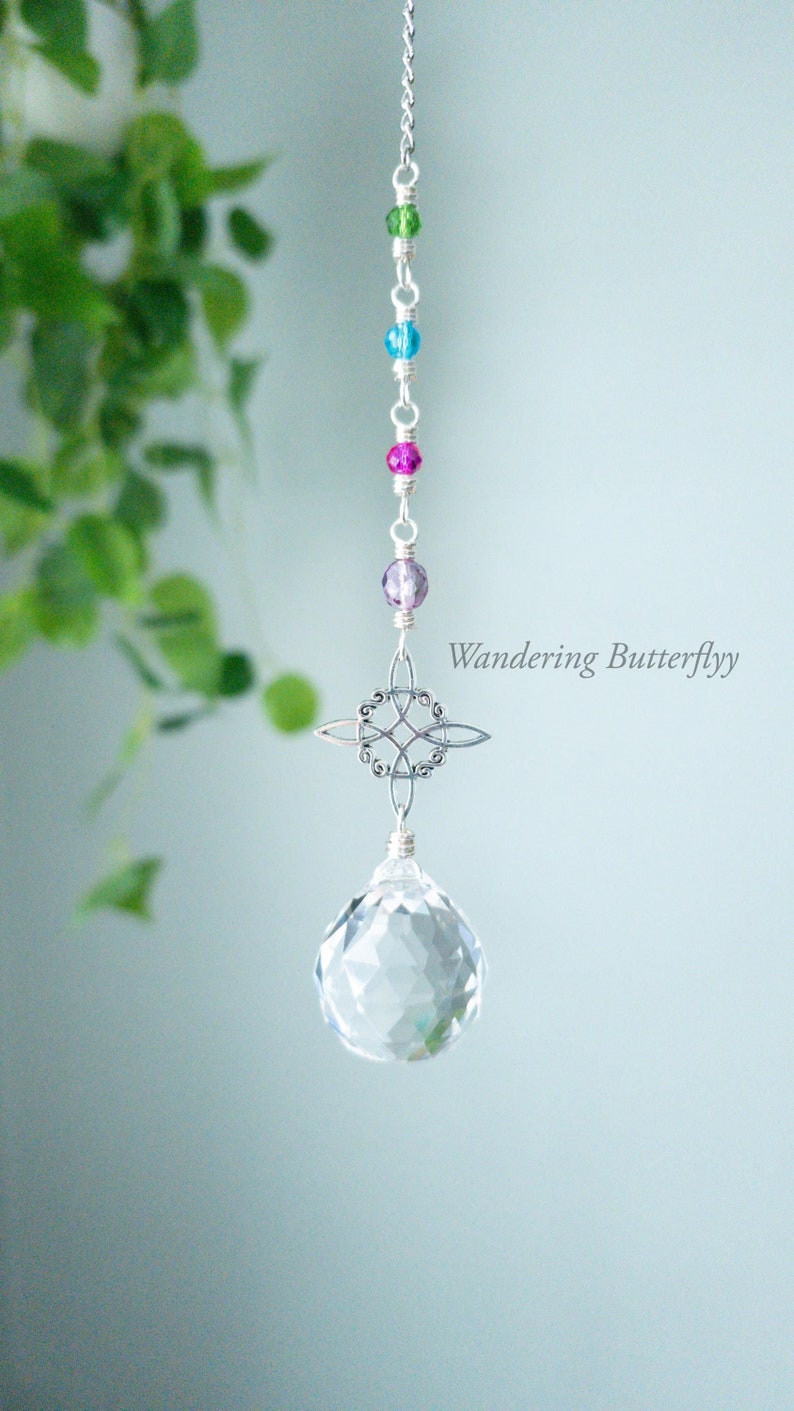 May include: A crystal suncatcher with a silver Celtic knot design and a clear crystal prism hanging from a silver chain with colorful beads. The beads are green, blue, pink, and purple.