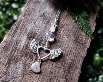 May include: Silver charm necklace with a heart and angel wings. The heart has the word "Mom" engraved on it. The necklace has pink and clear crystal beads.