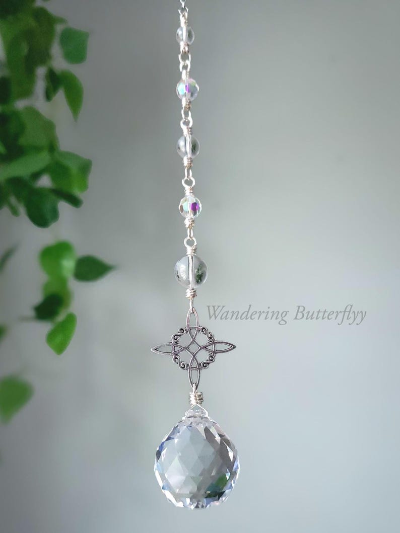 May include: A silver suncatcher with a faceted crystal ball. It has a Celtic knot design and iridescent beads. The text "Wandering Butterflyy" is visible. The suncatcher is designed to catch the light.