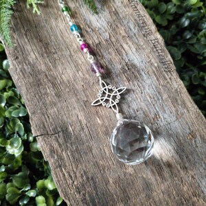 May include: A crystal suncatcher with a silver Celtic knot design and a clear crystal ball hanging from a silver chain with colorful beads.