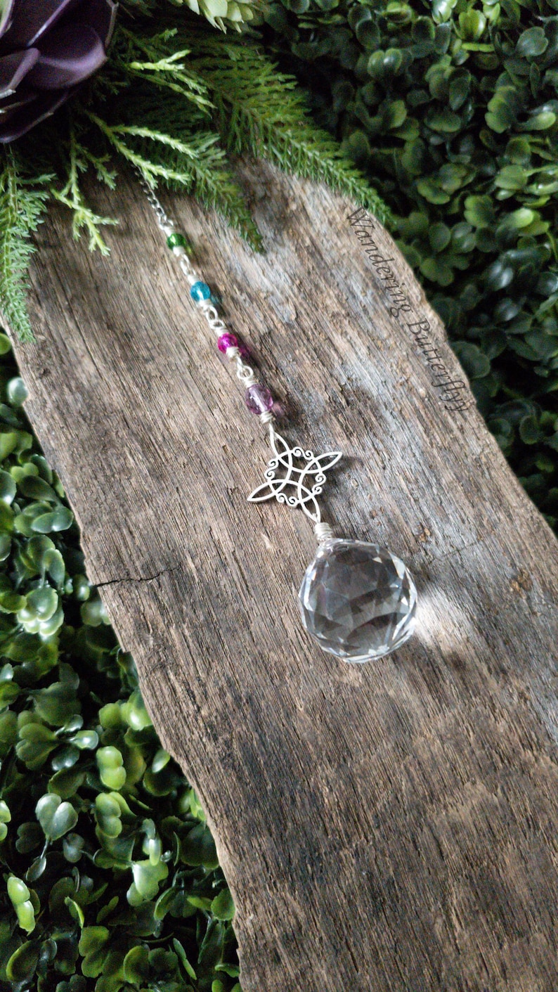 May include: A crystal suncatcher with a silver Celtic knot design and a clear crystal ball hanging from a silver chain with colorful beads.