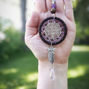 K&ouml;nnte beinhalten: Ein handgefertigter Traumf&auml;nger mit einem silbernen Lebensbaum-Design in der Mitte. Der Traumf&auml;nger hat einen dunkelbraunen gewebten Ring, verziert mit lila Perlen. Eine silberne Feder und ein klarer Kristall h&auml;ngen darunter. Der Text "Wandering Butterfly" ist sichtbar.