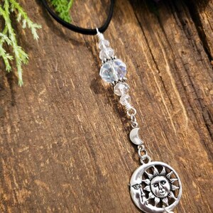 May include: A silver necklace with a sun and moon charm, crystal beads, and a black cord.
