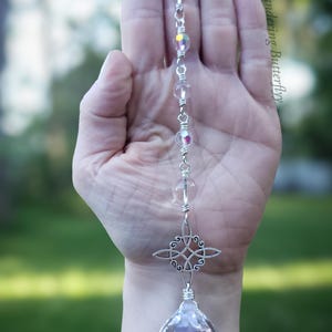 May include: A silver crystal suncatcher with a faceted crystal ball at the base. The suncatcher features clear and iridescent beads, and a decorative cross-shaped charm. The text "Wandering Butterfly" is visible in the background.